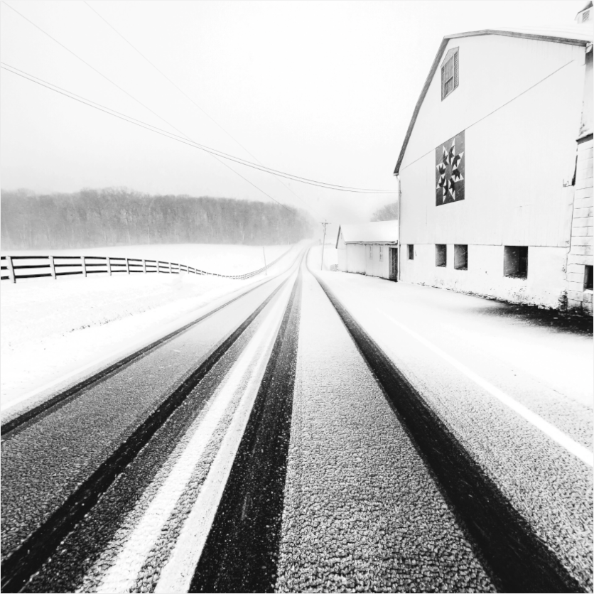 Black and white photograph of a rural road with converging lines—minimalist visual tension evokes mood, disorientation, and subconscious unease.