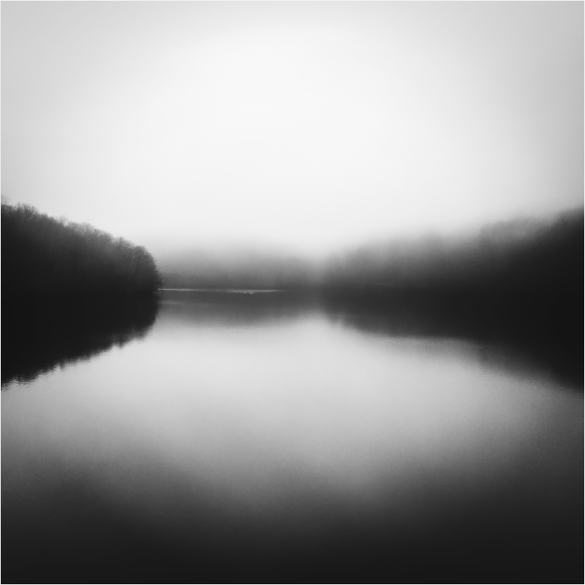 Black and white fine art photograph of a foggy field—diffuse light and tonal softness evoke stillness and early morning solitude.
