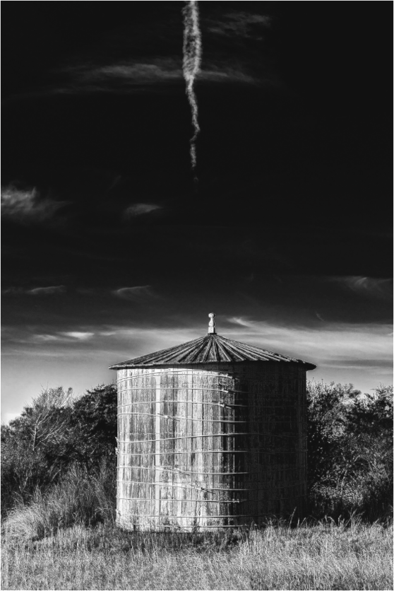Black and white photograph of a single fence post or rural marker—minimalist composition evoking elevation, ritual, and quiet significance.
