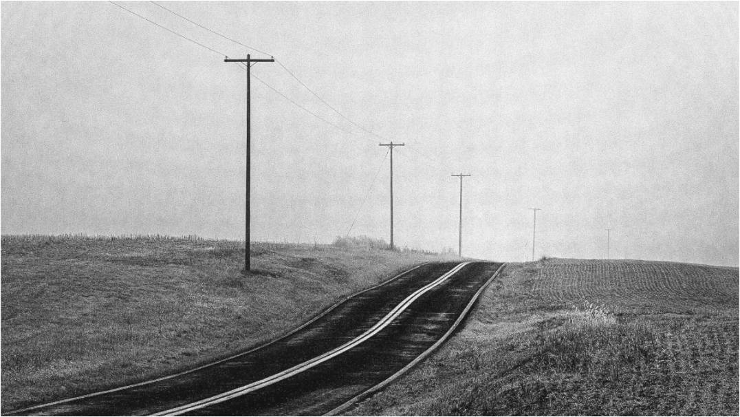 Black and white photograph of a rural road curving over a hill—minimalist landscape evoking the feeling of return, distance, and quiet longing.
