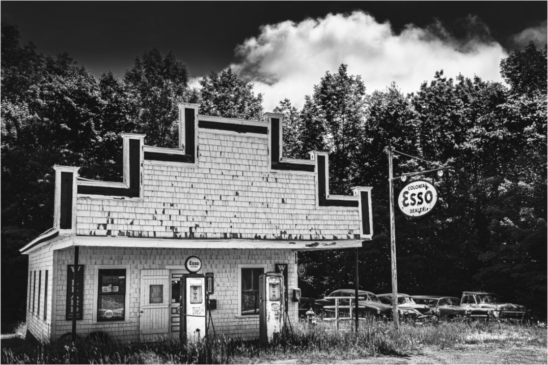 Black and white photograph of a vintage speed limit sign near a house—minimalist Americana image evoking contrast between motion and quiet.
